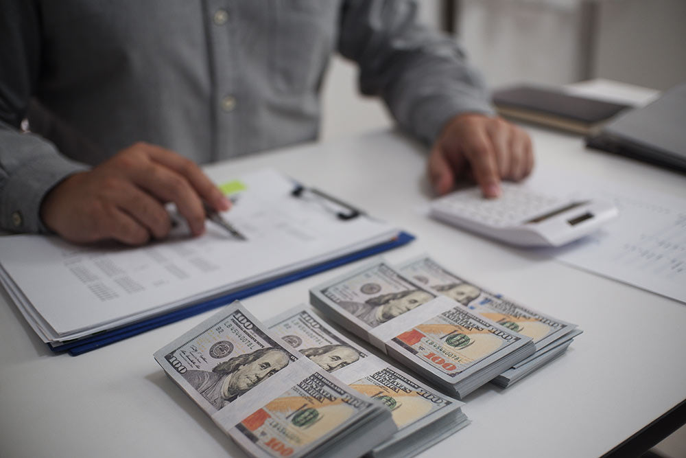 Person counting money with a calculator on a desk