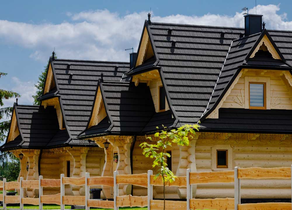 Wooden houses with black roofs and a wooden fence in front, under a blue sky.